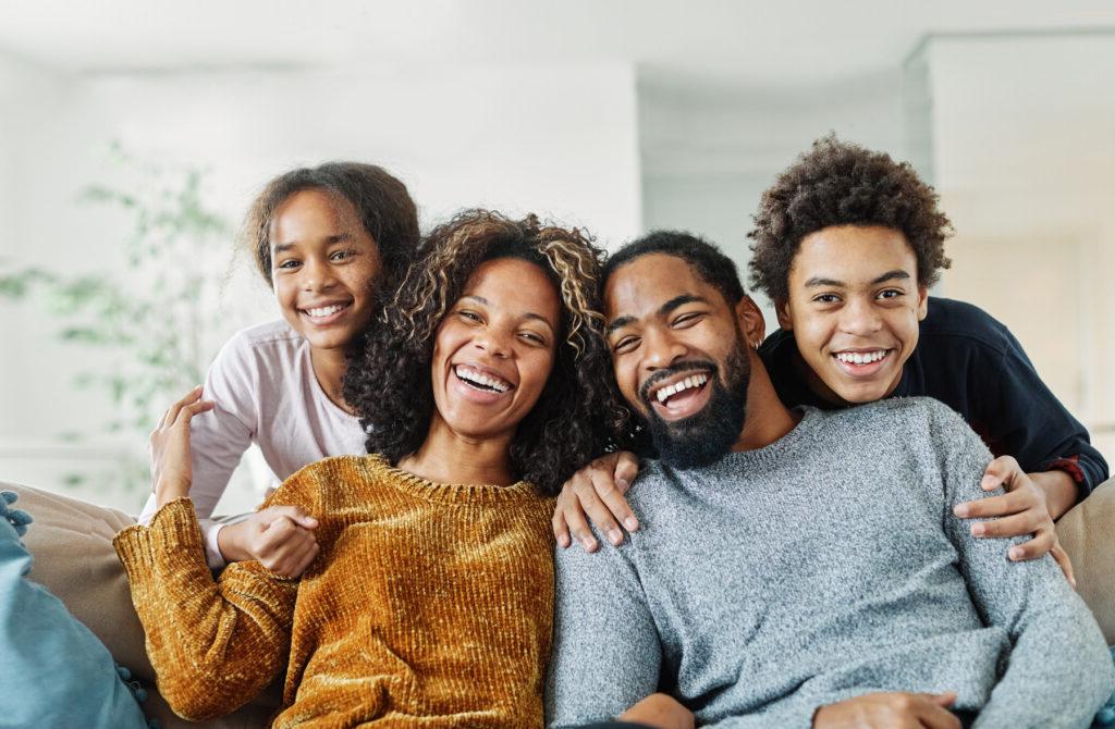 A family of four is sitting on their front porch smiling after opening a checking account at San Francisco Federal Credit Union.